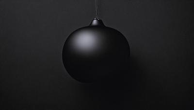 The primary subject of the image is a black sphere, which is hanging from a chain. The setting is a dark room, and the visual style appears to be a photo. The dominant colors are black and white, creating a moody atmosphere.