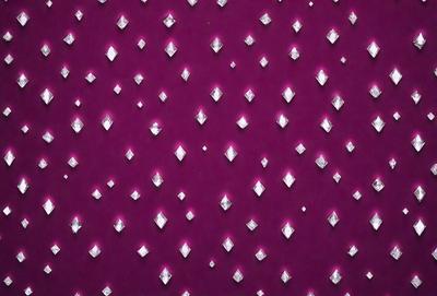 The primary subject of the image is a purple background with a pattern of small, round, pink crystals or diamond shapes. The setting appears to be a wall or a surface with a patterned design. The visual style of the image is a combination of a photo and digital art, as it features a close-up view of the patterned surface. The colors and mood of the image are predominantly purple and pink, creating a visually appealing and elegant atmosphere.