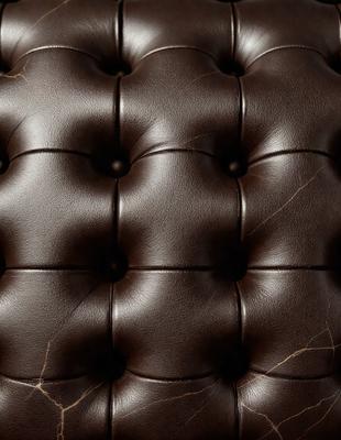 The primary subject of the image is a brown leather couch with a patterned design. The setting is a room with a brown background. The visual style is a close-up of the couch, showcasing its texture and pattern. The colors and mood of the image are warm and inviting, with the brown leather creating a cozy and comfortable atmosphere.