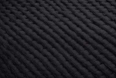 The primary subject of the image is a close-up of a black fabric with a pattern of interwoven lines. The setting is a black background, which contrasts with the fabric. The visual style is a close-up of the fabric, showcasing its intricate pattern. The colors and mood of the image are predominantly black, giving it a sleek and modern appearance.