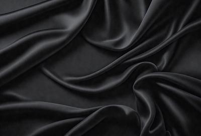 The primary subject of the image is a close-up of a black fabric, possibly a piece of clothing or a curtain. The setting is a dark background, which emphasizes the fabric's texture and details. The visual style appears to be a photo, as it captures the fabric's intricate patterns and textures. The colors and mood of the image are predominantly dark, with the black fabric serving as the focal point.