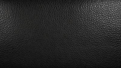 The primary subject of the image is a black leather material, which appears to be a leather jacket or a leather-like surface. The setting is a black background, which provides a contrasting and dramatic effect. The visual style is a close-up of the leather material, showcasing its texture and details. The colors and mood of the image are predominantly dark and moody, with the black leather material being the main focus.