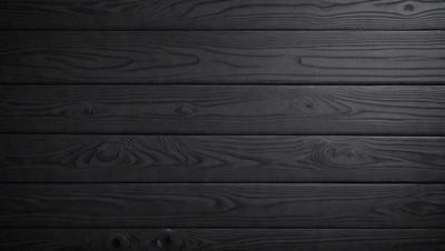 The primary subject of the image is a wooden wall with a black surface. The setting is a room with a black background, and the visual style is a photo. The dominant colors are black and brown, creating a moody atmosphere.