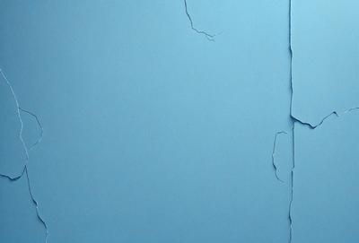 The primary subject of the image is a blue wall with a peeling paint surface. The setting is a room with a blue background. The visual style is a close-up of the peeling paint on the wall. The colors and mood of the image are predominantly blue, with a slightly distressed and aged appearance due to the peeling paint.
