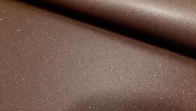 The primary subject of the image is a brown leather material, possibly a piece of leather or a leather-like fabric. The setting is a close-up view of the leather material, showcasing its texture and appearance. The visual style is a realistic representation of the leather material, with no indication of digital art, illustration, or clipart. The colors and mood of the image are predominantly brown, giving it a warm and natural atmosphere.