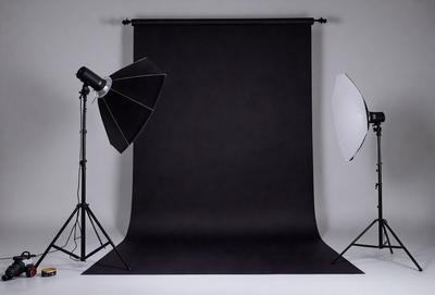 The primary subject of the image is a black background with a white light shining on it. The setting is a studio, and the visual style is a combination of photography and digital art. The dominant colors are black and white, creating a moody and dramatic atmosphere.