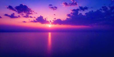 The primary subject of the image is the sunset, with the sun setting over the ocean. The setting is a vast body of water, and the visual style is a photo. The colors and mood of the image are predominantly warm and serene, with the sunset casting a warm glow over the ocean and the sky.