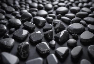 The primary subject of the image is a collection of black rocks. The setting is a black background, which creates a striking contrast with the rocks. The visual style is a close-up of the rocks, showcasing their unique shapes and textures. The colors and mood of the image are predominantly dark, with the black rocks being the main focus.