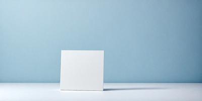 The primary subject of the image is a white square card sitting on a table. The setting is a blue wall, which serves as the backdrop for the card. The visual style is a photo, capturing the card in its natural environment. The colors and mood of the image are predominantly blue, creating a calm and serene atmosphere.