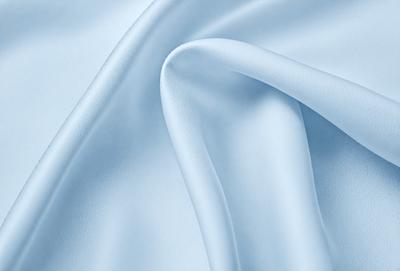 The primary subject of the image is a piece of white fabric, possibly a sheet or a curtain. The setting is a room with a blue background, which adds a contrasting color to the scene. The visual style is a close-up of the fabric, showcasing its texture and details. The colors and mood of the image are predominantly blue, creating a calm and serene atmosphere.