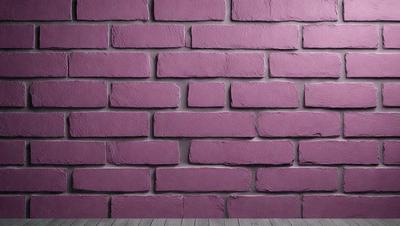 The primary subject of the image is a large brick wall painted in a pink hue. The setting is a room with a wooden floor, and the visual style appears to be a photo of the brick wall. The dominant colors in the image are pink and purple, creating a warm and inviting atmosphere.