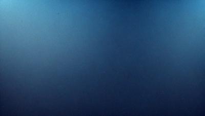 The primary subject of the image is a large, dark blue surface. The setting is a vast, empty space with no visible objects or backdrop. The visual style is a close-up of the blue surface, which gives the impression of a deep, dark ocean. The colors and mood of the image are predominantly dark and moody, with the blue surface creating a sense of depth and mystery.
