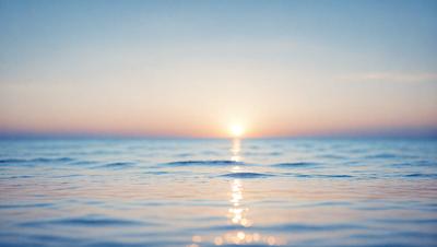 The primary subject of the image is the sunset, with the sun setting over the ocean. The setting is a vast body of water, and the visual style is a photo. The colors and mood of the image are predominantly warm and serene, as the sun casts its warm hues over the water and the sky.