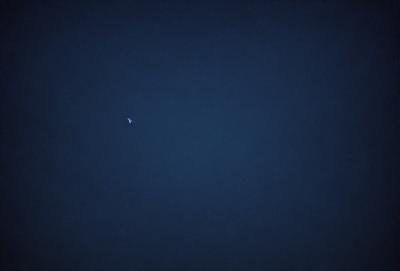 The primary subject of the image is a small, bright object in the sky. The setting is a dark, starry night with a clear view of the sky. The visual style is a photo, capturing the night sky with the small object as the focal point. The colors and mood of the image are predominantly dark, with the small object standing out as a bright, luminous point in the night sky.