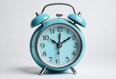 The primary subject of the image is a blue alarm clock with a white face. The clock is placed on a white surface, which serves as the background. The visual style of the image is a photo, capturing the details of the alarm clock. The dominant colors in the image are blue and white, creating a calm and soothing atmosphere.