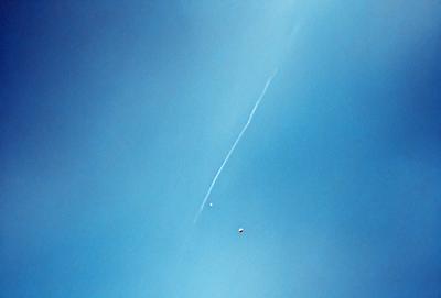 The primary subject of the image is a rocket flying through the sky. The setting is a clear blue sky, and the visual style is a photo. The colors are predominantly blue, and the mood is one of excitement and adventure.