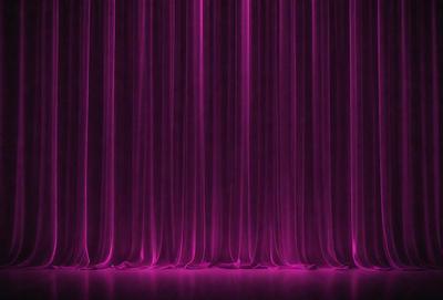The primary subject of the image is a purple curtain, which is the main object, scene, or focus of the image. The setting is a stage or a theater, as the curtain is hanging on a stage. The visual style is a photo, and the dominant colors are purple and pink, creating a warm and inviting atmosphere.