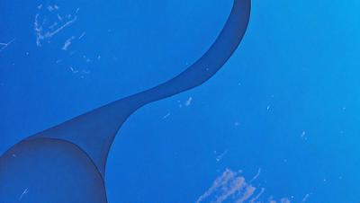 The primary subject of the image is a large, curved metal structure that resembles a blue spiral. The setting is a clear blue sky, and the visual style appears to be a combination of a photo and a digital art or illustration. The colors and mood of the image are predominantly blue, creating a serene and calming atmosphere.