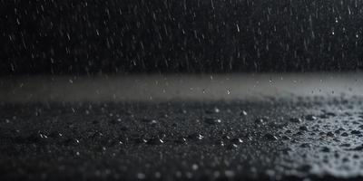 The primary subject of the image is a rainy street scene. The setting is a wet road with rain falling, creating a dark and moody atmosphere. The visual style is a photo, capturing the rainy weather and the wet road. The colors are predominantly dark, with the rain creating a sense of gloominess.