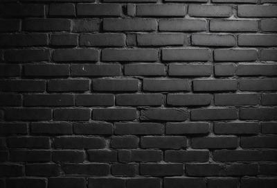 The primary subject of the image is a brick wall. The setting is a dark room, and the visual style is a black and white photo. The dominant colors are black and white, creating a moody atmosphere.