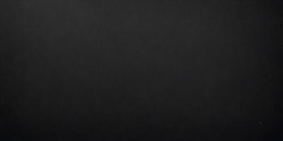 The primary subject of the image is a black leather surface. The setting is a dark room, and the visual style is a close-up of the leather surface. The colors and mood of the image are predominantly dark and moody, with the black leather being the main focus.