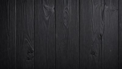 The primary subject of the image is a wooden wall with a black surface. The setting is a room with a black background. The visual style is a close-up of the wooden wall, showcasing its texture and details. The colors and mood of the image are dark and moody, with the black wooden wall creating a dramatic and intense atmosphere.