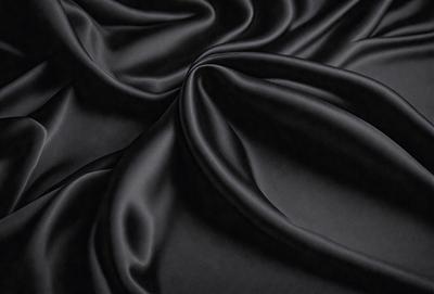The primary subject of the image is a close-up of a black fabric, possibly a piece of silk or velvet. The setting is a dark background, which emphasizes the fabric's texture and color. The visual style is a close-up, focusing on the details of the fabric. The colors and mood of the image are predominantly dark, with the black fabric being the main focus.