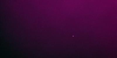 The image features a purple background with a small, bright light in the middle. The light appears to be a star, and it is the primary subject of the image. The setting is a dark, purple sky, which contrasts with the bright light. The visual style is a combination of a photo and a digital art, creating a unique and captivating scene. The colors and mood of the image are predominantly purple, with the bright light adding a touch of warmth and contrast to the overall atmosphere.
