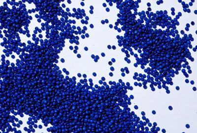 The primary subject of the image is a large pile of blue beads. The beads are scattered across a white surface, creating a visually striking contrast. The setting appears to be a workspace or a display area for the beads. The visual style of the image is a close-up of the beads, showcasing their vibrant color and unique texture. The overall atmosphere of the image is one of creativity and craftsmanship, as the beads are likely used in various artistic projects or as decorative elements.