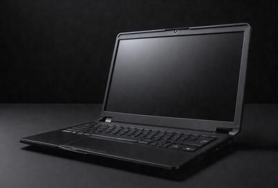 The primary subject of the image is a laptop computer. The laptop is sitting on a black surface, which could be a table or a desk. The visual style of the image is a photo, capturing the laptop in a close-up view. The colors and mood of the image are dark and moody, with the laptop being the main focus of the scene.