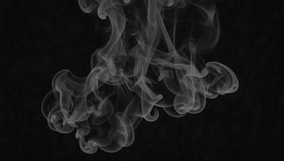 The primary subject of the image is a cloud of smoke, which is the main object, scene, or focus of the image. The setting is a dark background, which creates a dramatic and moody atmosphere. The visual style is a black and white photo, which adds a classic and timeless quality to the image. The colors and mood are dominated by the smoke, which appears as a dense and swirling mass, creating a sense of mystery and intrigue.