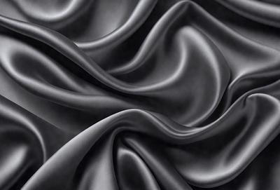 The primary subject of the image is a close-up of a black fabric, possibly a piece of clothing or a curtain. The setting is a dark background, which emphasizes the fabric's texture and pattern. The visual style appears to be a photo, as the fabric is captured in detail. The colors and mood of the image are predominantly dark, with the black fabric being the main focus.