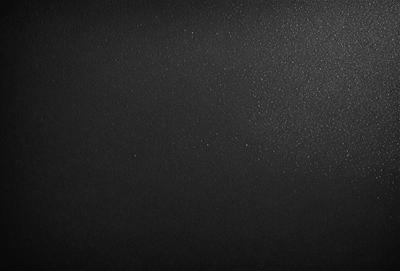 The primary subject of the image is a black background with a few white specks. The setting is a dark room, and the visual style is a close-up of the black background. The colors and mood of the image are predominantly dark and moody, with the white specks adding a touch of contrast.