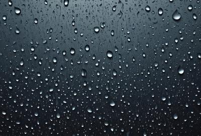 The primary subject of the image is a rainy day, as seen through a window. The setting is a dark, cloudy sky, and the visual style is a photo. The colors and mood of the image are dominated by the rain, with the drops creating a moist and atmospheric scene.