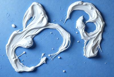 The primary subject of the image is a blue surface with white paint dripping on it. The setting appears to be a workspace or an artistic environment. The visual style of the image is a combination of photo and digital art, as it captures the dripping paint in a realistic manner. The colors in the image are predominantly blue and white, creating a calm and serene atmosphere.