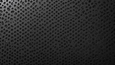 The primary subject of the image is a black background with a pattern of small holes. The setting is a dark room, and the visual style is a close-up of the pattern. The dominant colors are black and white, and the overall atmosphere is a mix of modern and industrial.