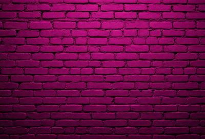 The primary subject of the image is a brick wall with a purple hue. The setting is a brick wall, and the visual style is a photo. The dominant colors are purple and pink, creating a warm and inviting atmosphere.