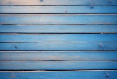 The primary subject of the image is a wooden wall with a blue color. The setting is a room with a wooden surface, and the visual style is a close-up of the wooden wall. The dominant colors are blue and brown, creating a calm and serene atmosphere.