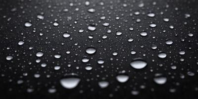 The primary subject of the image is a close-up of a black surface with water droplets on it. The setting is a dark background, and the visual style appears to be a photo. The colors in the image are predominantly black and white, with the water droplets adding a touch of gray. The overall atmosphere is moist and reflective, as the water droplets create a sense of depth and texture on the black surface.