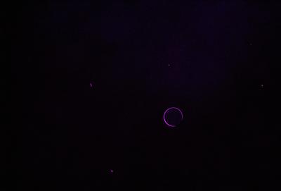 The image is a black and purple digital art piece featuring a large, glowing circle in the center of the frame. The circle is surrounded by a few smaller circles, creating a visually striking composition. The overall atmosphere of the image is dark and mysterious, with the purple hues adding a sense of depth and intrigue.