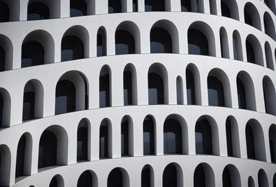 The primary subject of the image is a tall, white building with many windows. The building is made of white bricks, giving it a unique and modern appearance. The setting is a cityscape, with the building standing tall against the urban backdrop. The visual style of the image is a photo, capturing the details and textures of the building and its surroundings. The colors and mood of the image are predominantly white, giving it a clean and minimalist feel.