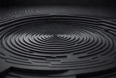 The primary subject of the image is a black and white spiral pattern. The setting is a dark background, which contrasts with the spiral pattern. The visual style is a close-up of the spiral pattern, showcasing its intricate details. The colors and mood of the image are predominantly dark and moody, with the spiral pattern being the main focal point.