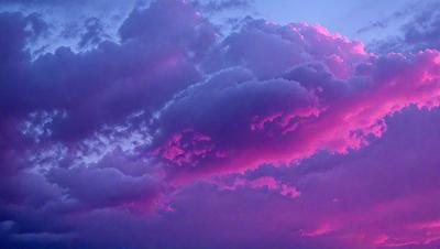 The primary subject of the image is a cloudy sky with pink and purple hues. The setting is a cloudy day, and the visual style is a natural, outdoor scene. The colors and mood of the image are predominantly pink and purple, creating a serene and calming atmosphere.
