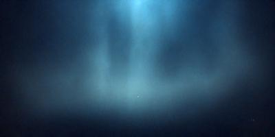 The primary subject of the image is a blue sky with a few clouds. The setting is a dark blue background, which creates a contrast with the clouds. The visual style is a photo, capturing the natural beauty of the sky. The colors and mood of the image are predominantly dark and moody, with the blue sky and clouds creating a sense of depth and tranquility.