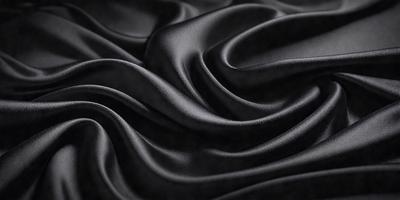 The primary subject of the image is a close-up of a black fabric, possibly a piece of silk or velvet. The setting is a black background, which emphasizes the fabric's texture and pattern. The visual style is a close-up, focusing on the details of the fabric. The colors and mood of the image are predominantly black, creating a dramatic and sophisticated atmosphere.