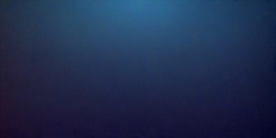 The primary subject of the image is a large body of water, which appears to be a deep blue ocean. The setting is a vast expanse of water, with no visible land or other objects. The visual style of the image is a close-up of the water, showcasing its depth and color. The colors and mood of the image are predominantly dark and moody, with the deep blue water creating a sense of vastness and tranquility.