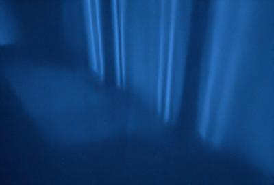 The primary subject of the image is a person's hand, which is captured in a blue-tinted photo. The setting is a room with a blue wall, and the visual style is a close-up of the hand. The colors and mood of the image are predominantly blue, creating a calm and serene atmosphere.