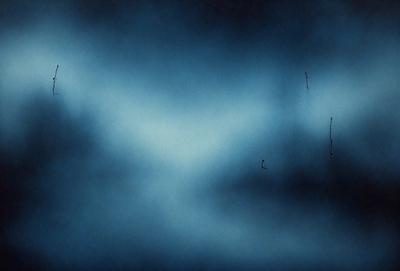 The primary subject of the image is a blue sky with a few clouds. The setting is a dark blue background, which creates a contrasting effect with the clouds. The visual style appears to be a photo, as it captures the natural beauty of the sky. The colors and mood of the image are predominantly dark and moody, with the blue sky and clouds creating a sense of depth and tranquility.