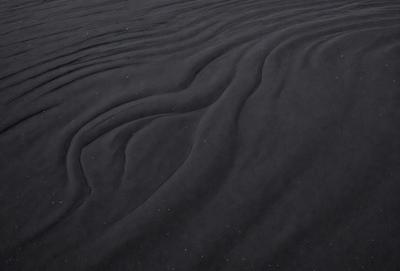 The image features a black and white scene of a sandy beach with a sandy surface. The primary subject is a close-up of the sand, showcasing its texture and patterns. The setting is a beach environment, and the visual style is a photo. The colors and mood of the image are predominantly black and white, giving it a classic and timeless appearance.