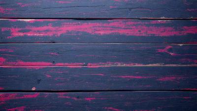 The primary subject of the image is a wooden wall with a purple paint on it. The setting is a room with a wooden floor. The visual style is a close-up of the wooden wall, showcasing the purple paint. The colors and mood of the image are predominantly purple, creating a unique and artistic atmosphere.